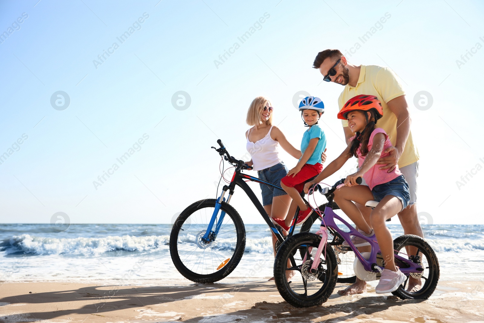 Photo of Happy parents teaching children to ride bicycles on sandy beach near sea