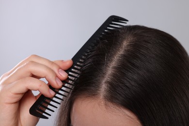 Photo of Woman with comb examining her hair and scalp on grey background, closeup