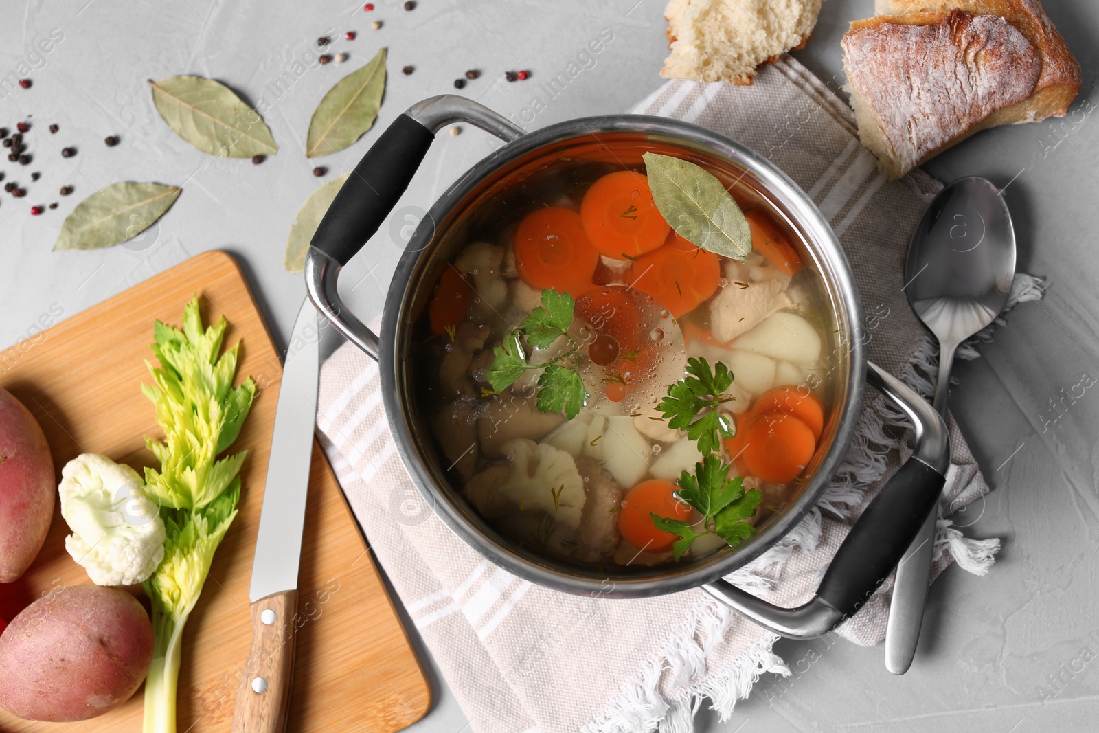 Photo of Pot of delicious vegetable bouillon and ingredients on light grey table, flat lay