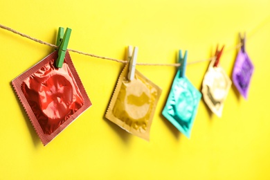 Photo of Colorful condoms hanging on clothesline against yellow background. Safe sex concept