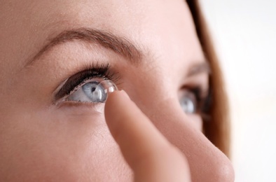 Photo of Young woman putting contact lens in her eye on light background, closeup