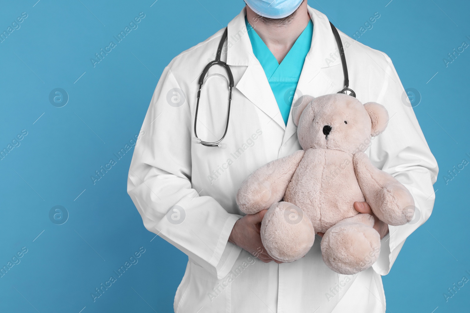 Photo of Pediatrician with teddy bear and stethoscope on light blue background, closeup