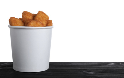 Photo of Bucket with tasty chicken nuggets on black wooden table against white background. Space for text