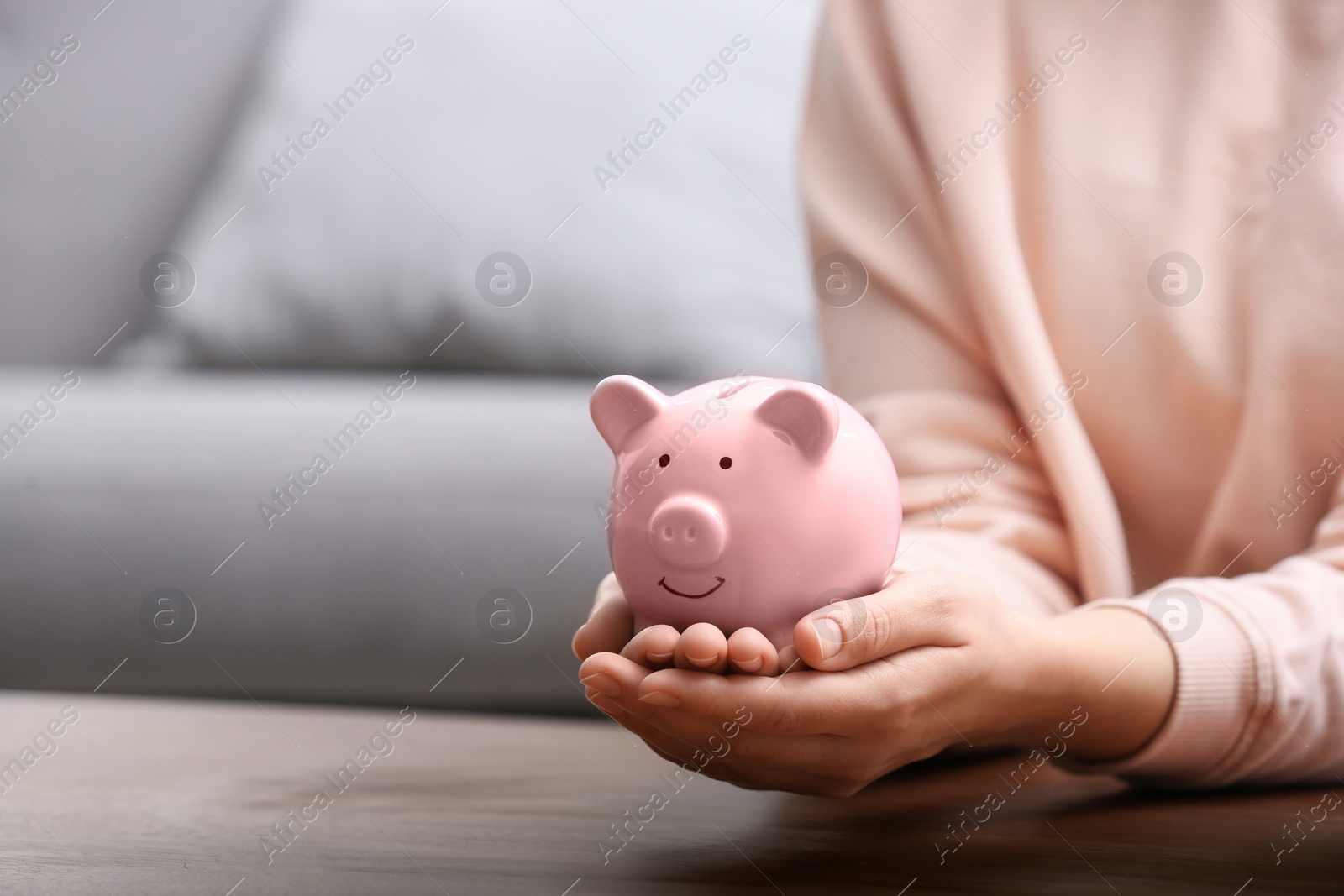 Photo of Woman with piggy bank at wooden table, closeup. Space for text