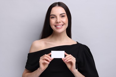 Happy woman holding blank business card on light grey background