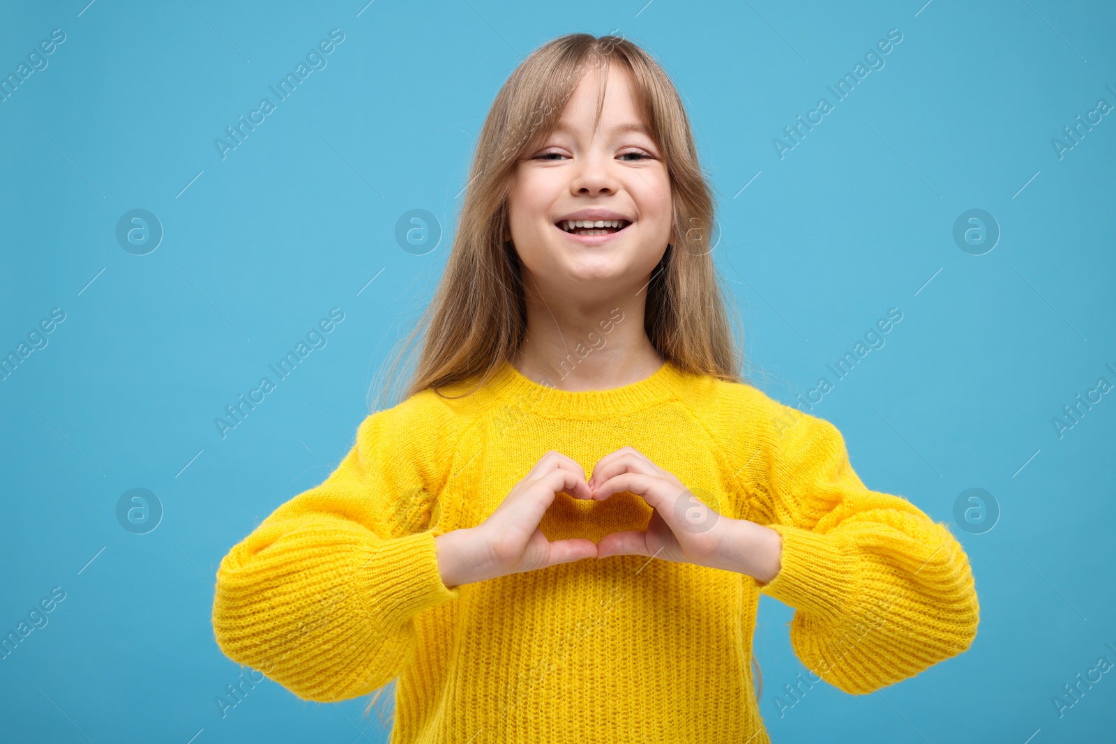 Photo of Happy girl showing heart gesture with hands on light blue background