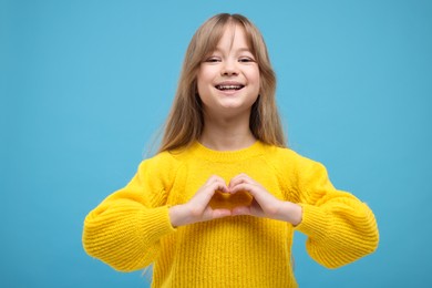 Photo of Happy girl showing heart gesture with hands on light blue background