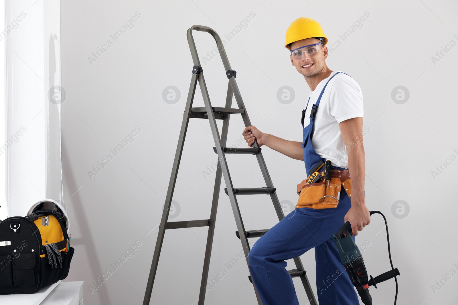 Photo of Worker with electric drill on ladder indoors