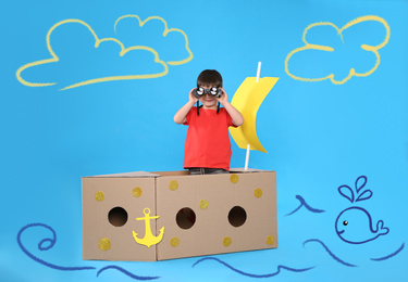 Cute little child playing in cardboard ship on light blue background with illustrations