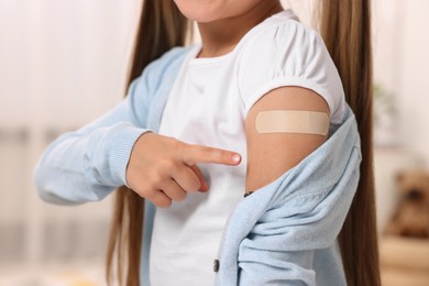 Photo of Girl pointing at sticking plaster after vaccination on her arm indoors, closeup