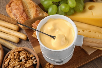 Photo of Pot of tasty cheese fondue and fork with bread on wooden table