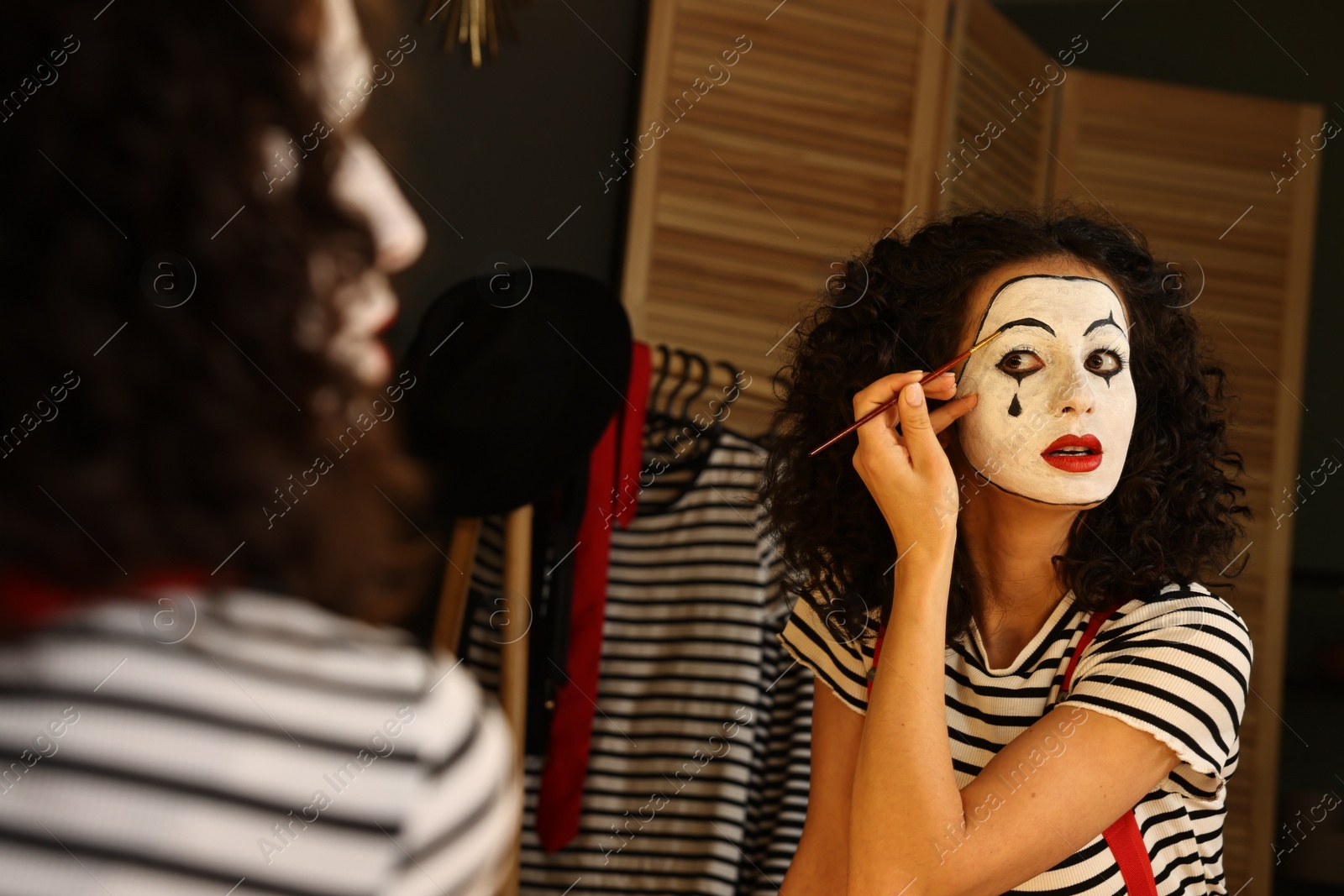 Photo of Young woman applying mime makeup near mirror indoors