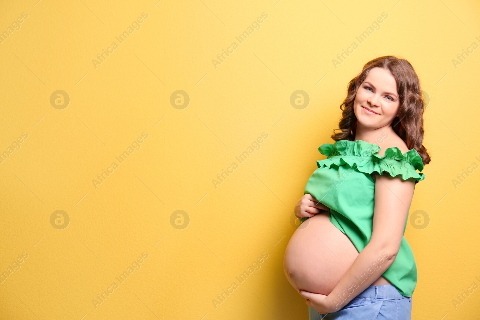 Photo of Young pregnant woman in casual clothes on color background