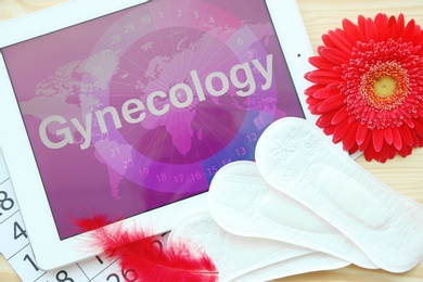 Photo of Flat lay composition with tablet, menstrual pads and flower on wooden background. Gynecological checkup