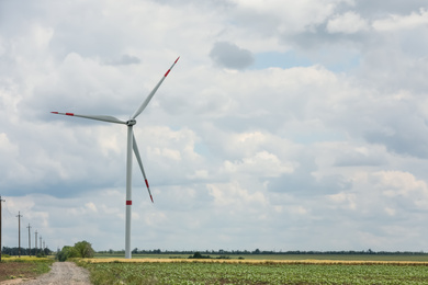 Photo of Modern wind turbine in field on cloudy day. Alternative energy source