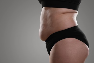 Woman with excessive belly fat on grey background, closeup. Overweight problem