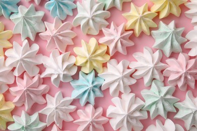 Many tasty meringue cookies on pink background, flat lay