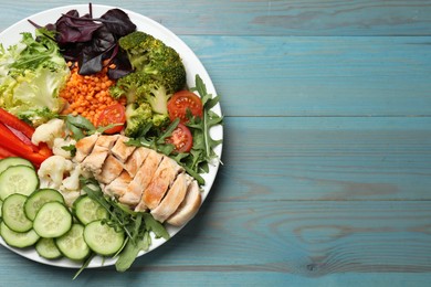 Balanced diet and healthy foods. Plate with different delicious products on light blue wooden table, top view. Space for text