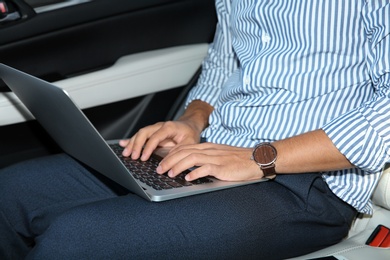 Photo of Man using modern laptop in car, focus on hands