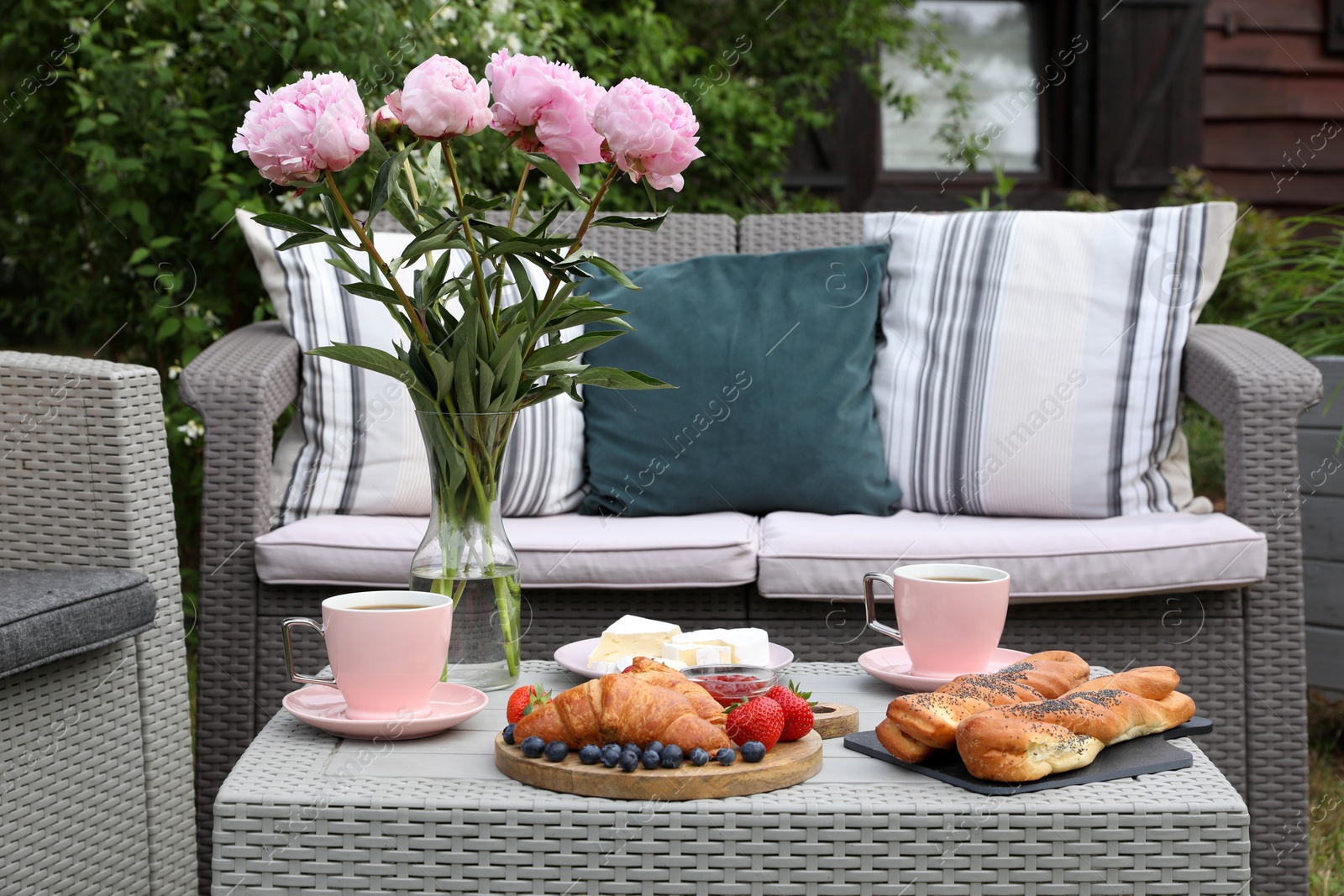 Morning drink, pastry, berries, cheese and vase with flowers on rattan table. Summer breakfast outdoors Photo of Morning drink, pastry, berries, cheese and vase with flowers on rattan table. Summer breakfast outdoors