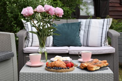 Photo of Morning drink, pastry, berries, cheese and vase with flowers on rattan table. Summer breakfast outdoors