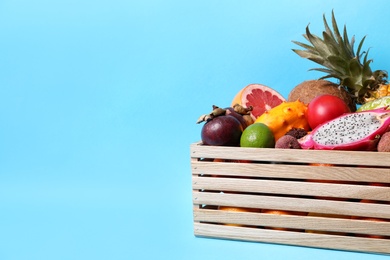 Different tropical fruits in wooden box on light blue background. Space for text