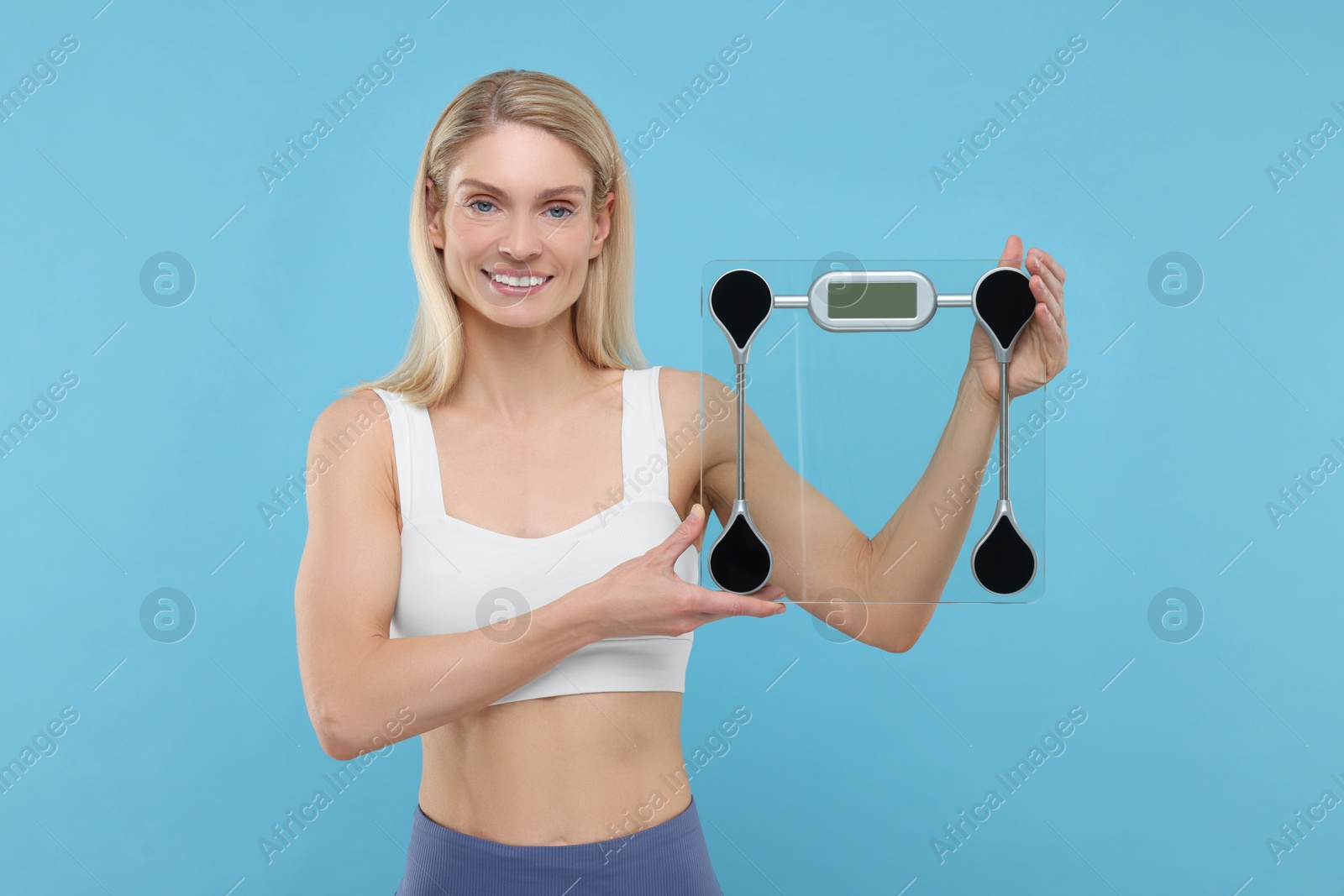 Photo of Slim woman holding scales on light blue background. Weight loss