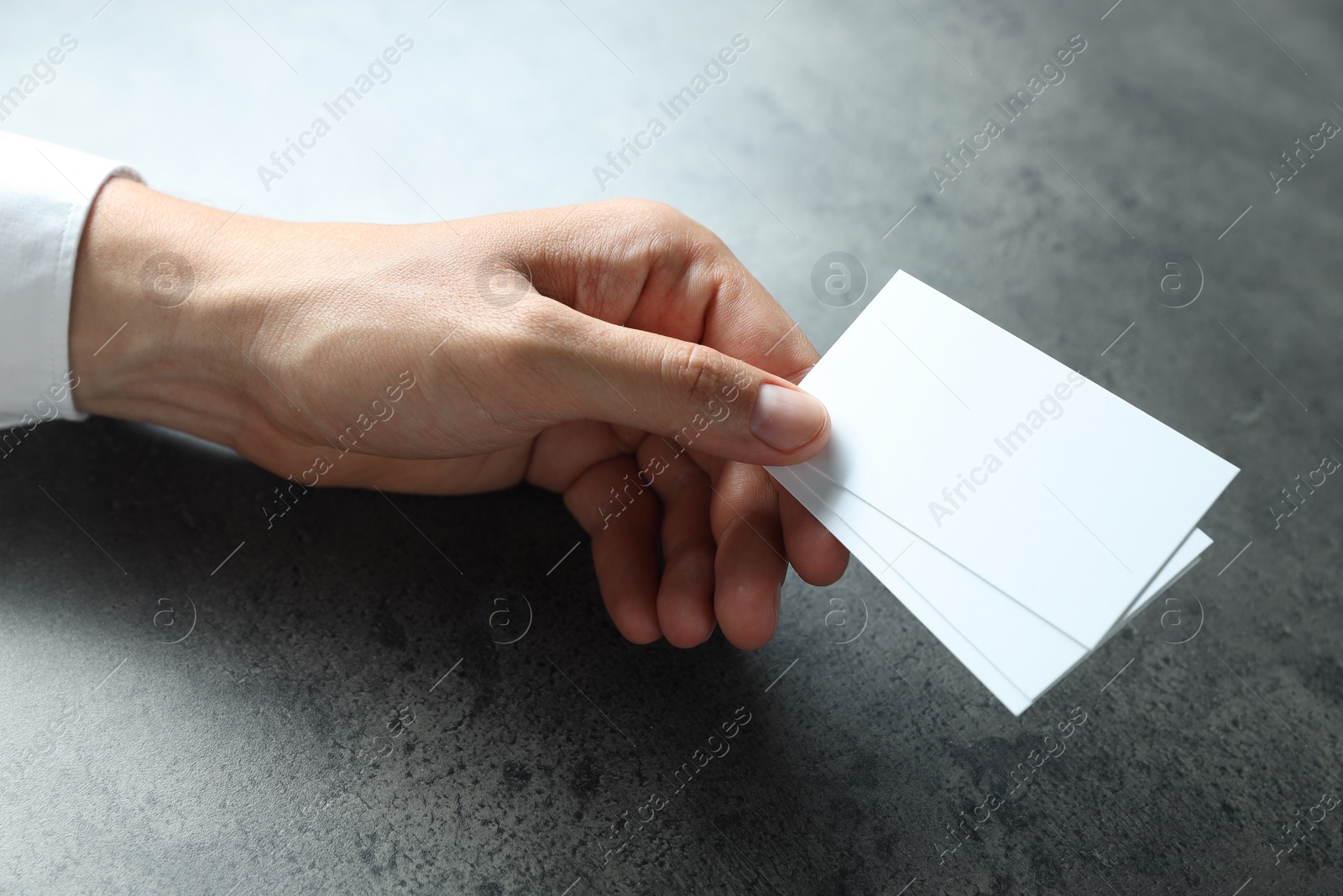 Photo of Man holding blank cards at black textured table, closeup. Mockup for design