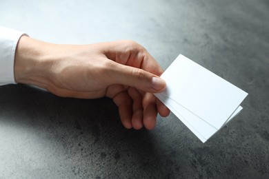 Photo of Man holding blank cards at black textured table, closeup. Mockup for design