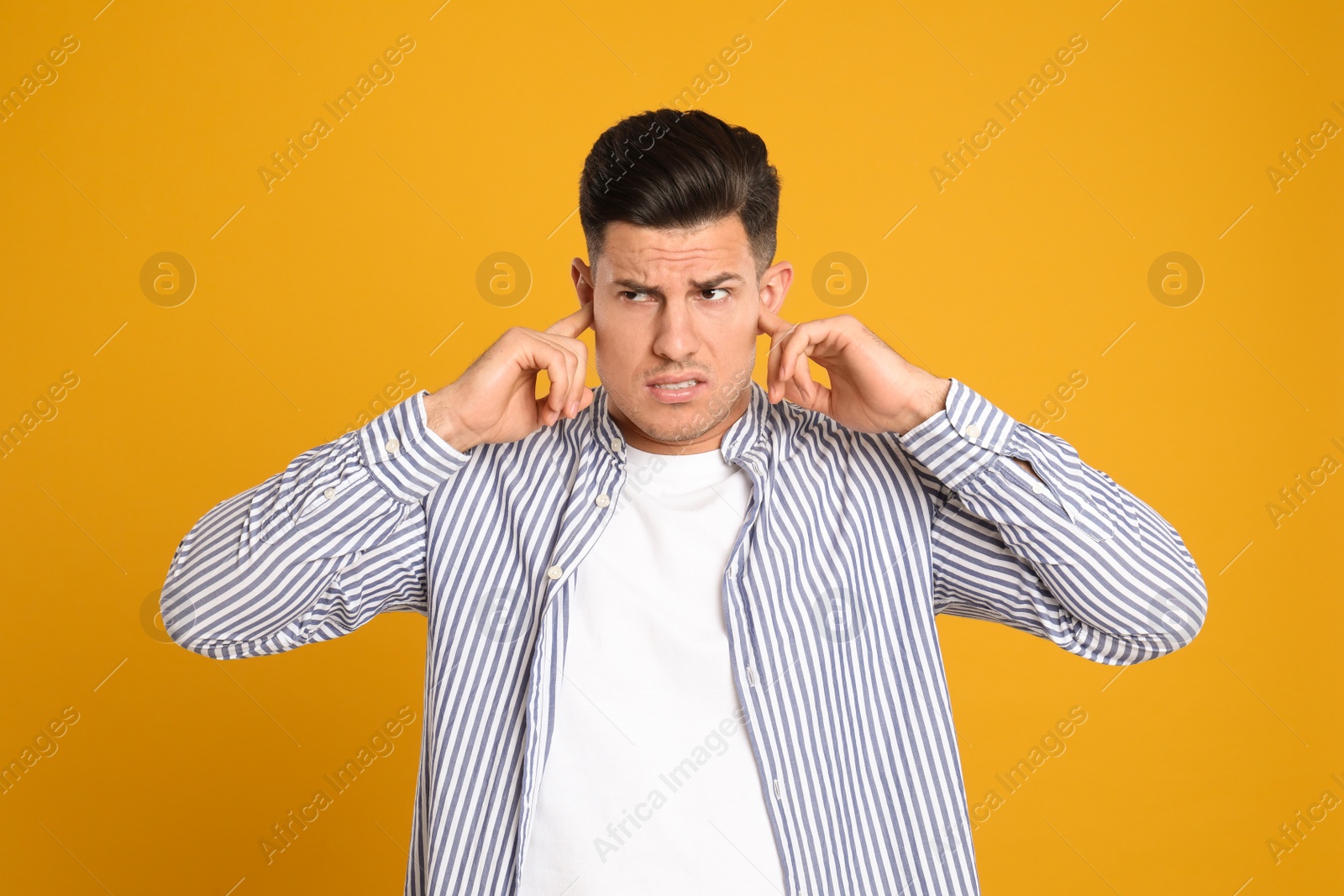 Photo of Man covering ears with fingers on yellow background