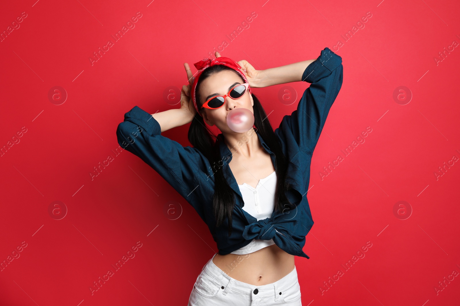 Photo of Fashionable young woman in pin up outfit blowing bubblegum on red background