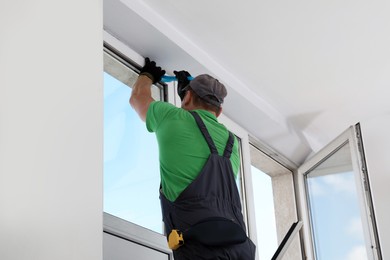 Worker in uniform installing window indoors, back view