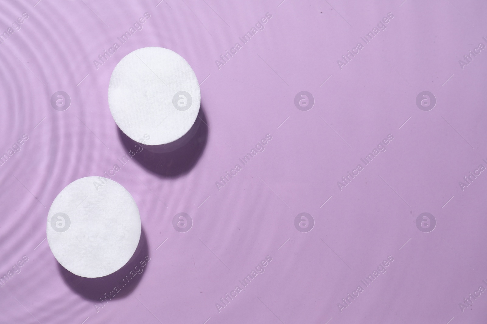 Photo of Cotton pads in micellar water on violet background, top view. Space for text