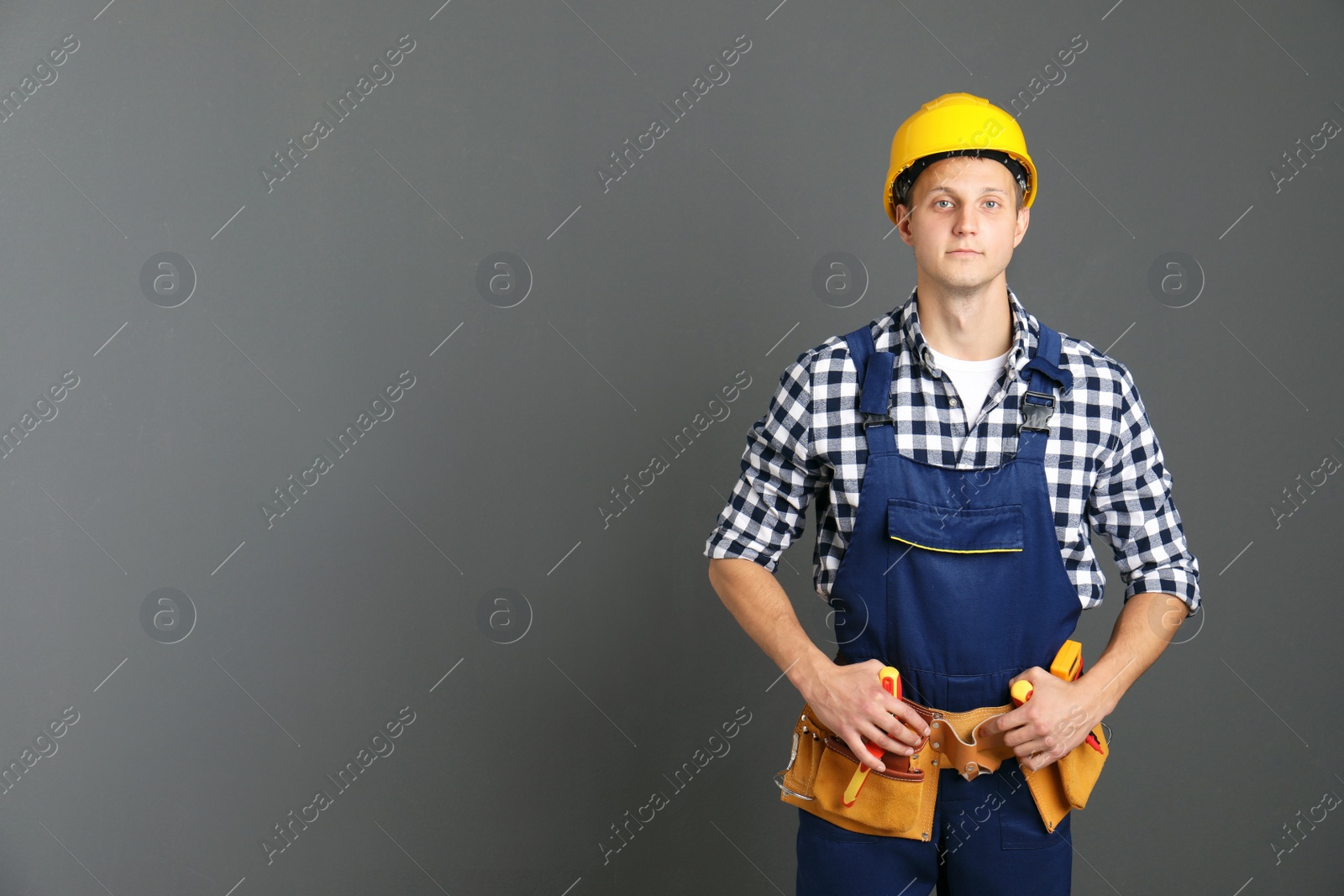 Photo of Electrician with tools wearing uniform on gray background. Space for text