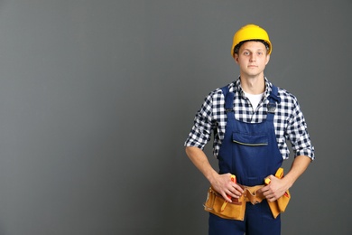 Electrician with tools wearing uniform on gray background. Space for text