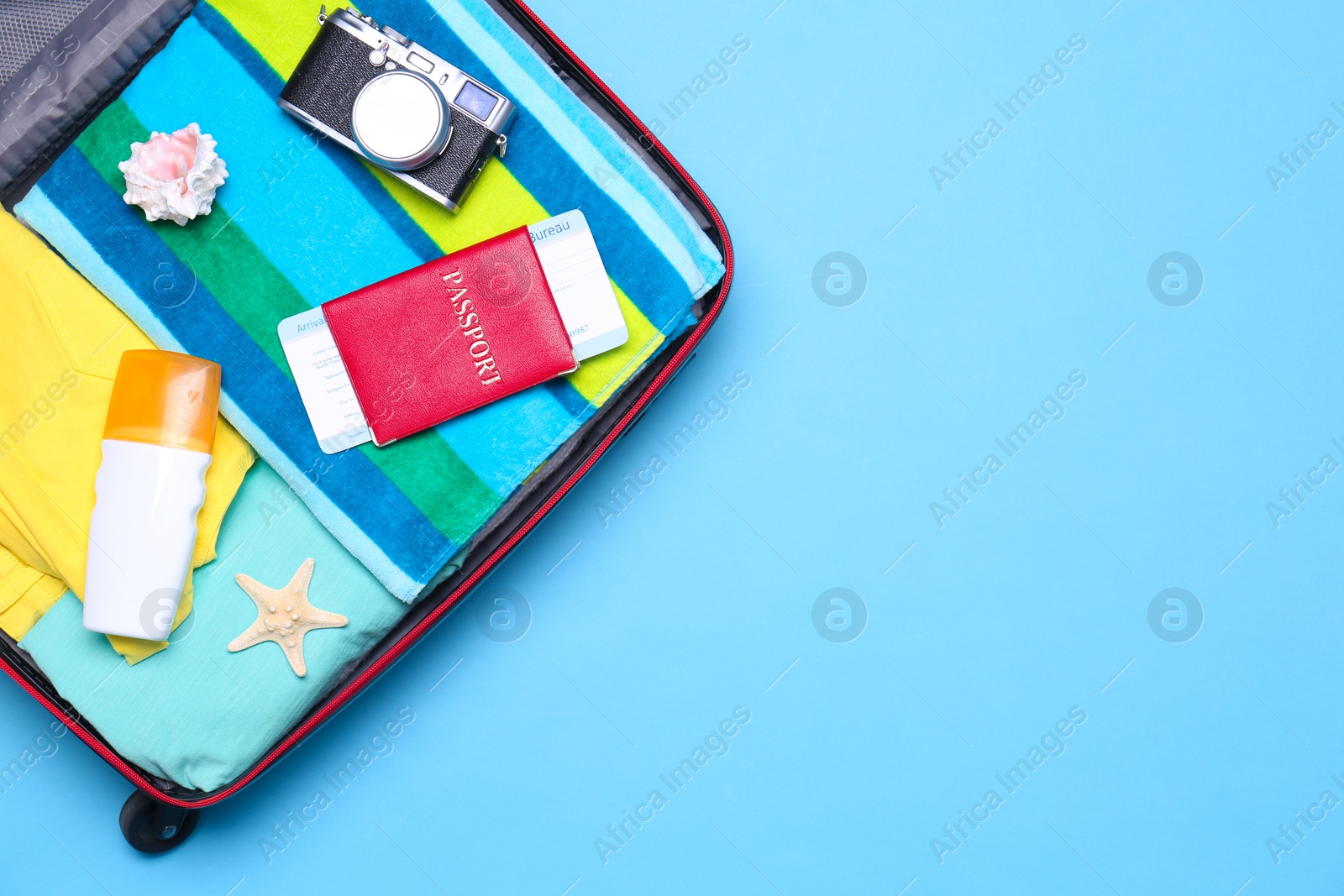 Photo of Open suitcase with beach objects on blue background, top view. Space for text