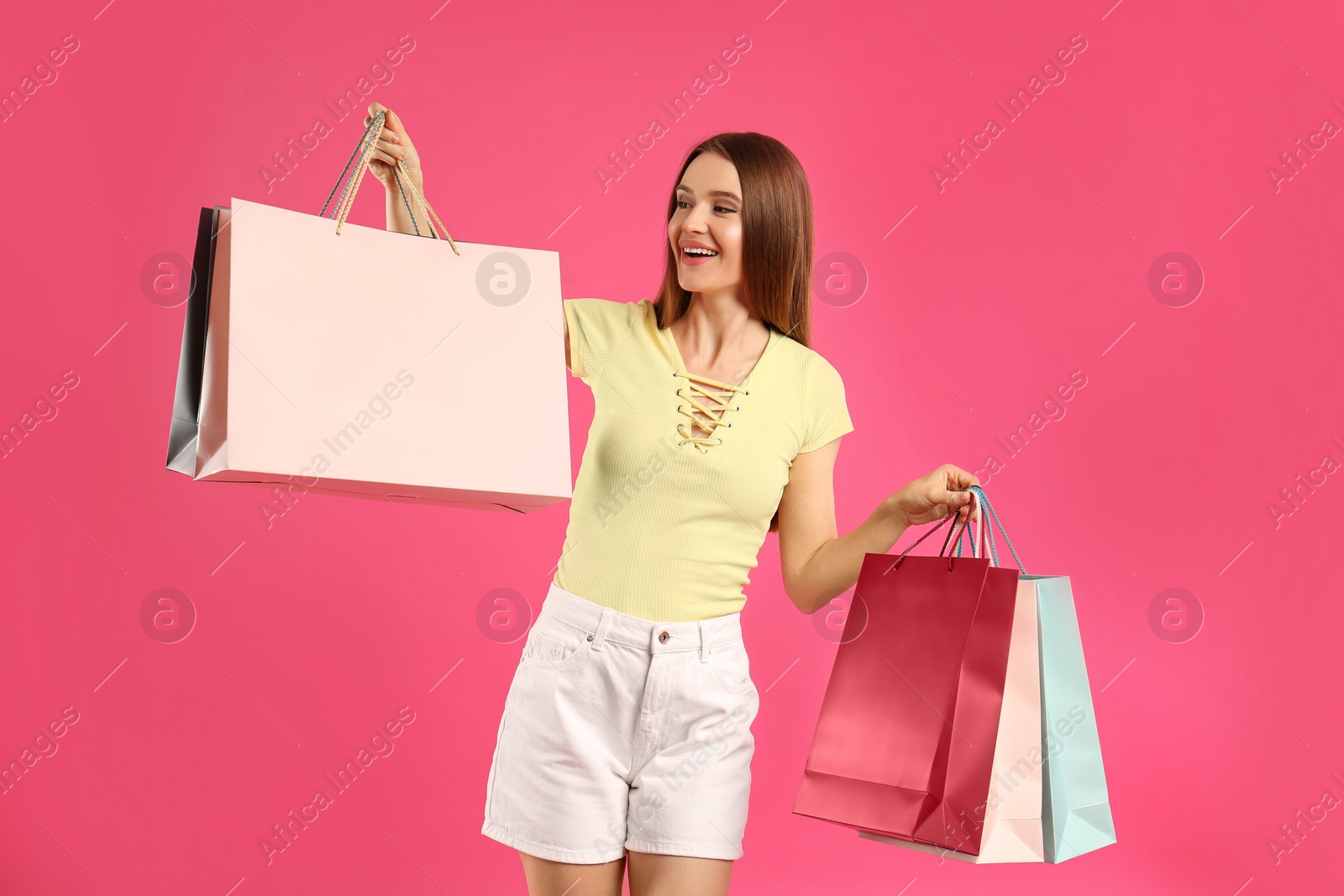 Photo of Beautiful young woman with paper shopping bags on pink background