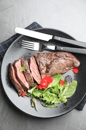 Delicious grilled beef meat served with greens on grey table, top view