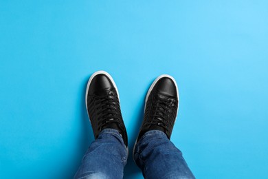 Man in stylish sneakers standing on light blue background, top view