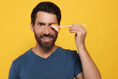 Funny man holding sushi with chopsticks on orange background