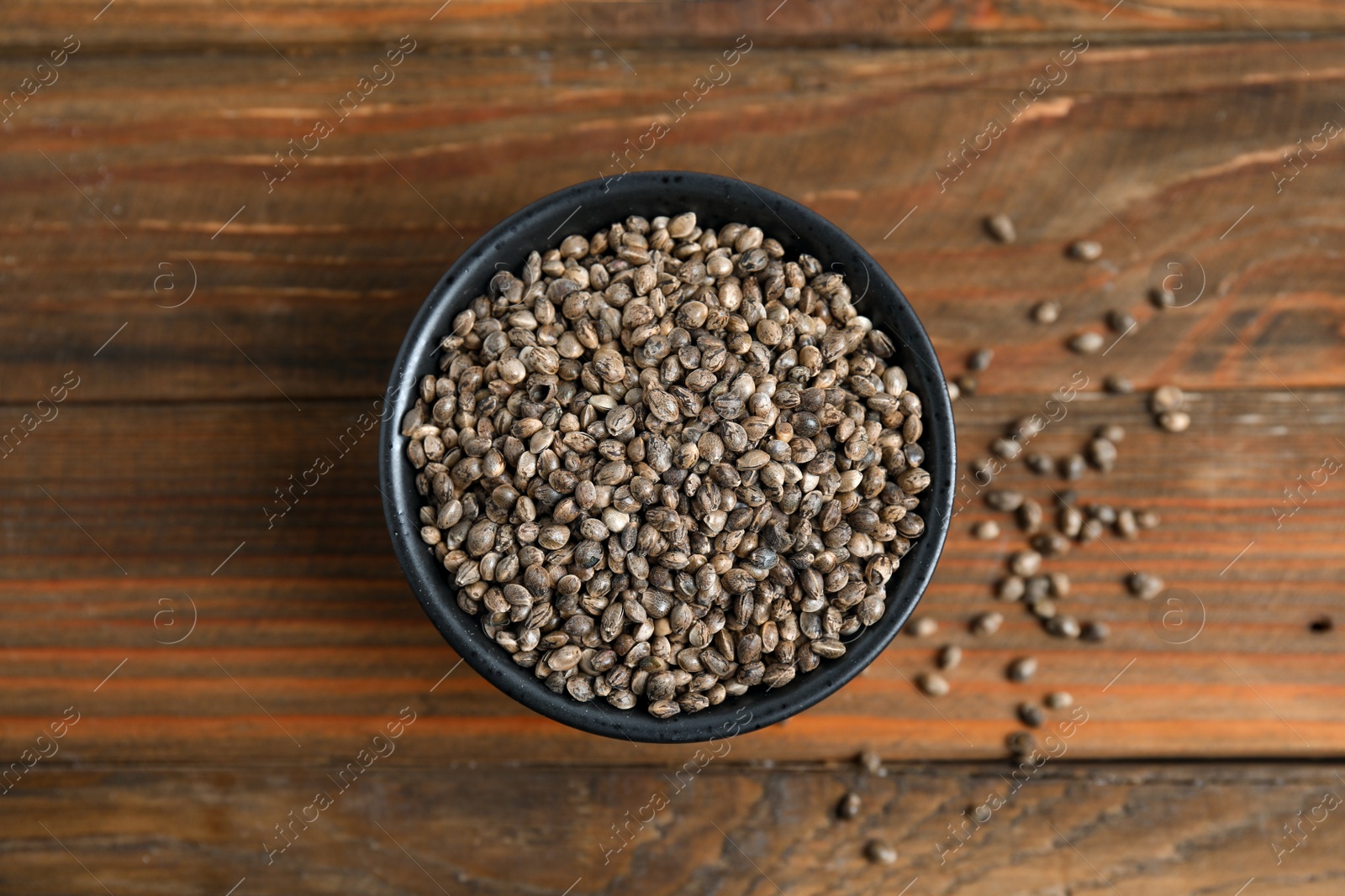 Photo of Bowl with organic hemp seeds on wooden table, flat lay