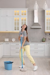 Photo of Enjoying cleaning. Happy woman with mop listening music in kitchen