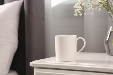 Photo of Ceramic mug on white bedside table indoors. Mockup for design