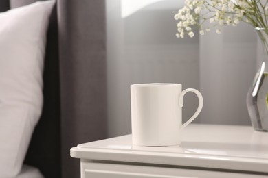 Ceramic mug on white bedside table indoors. Mockup for design