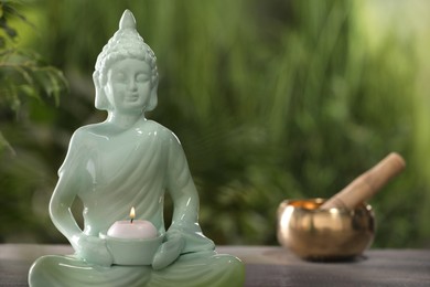 Photo of Buddhism religion. Decorative Buddha statue with burning candle on table outdoors, space for text