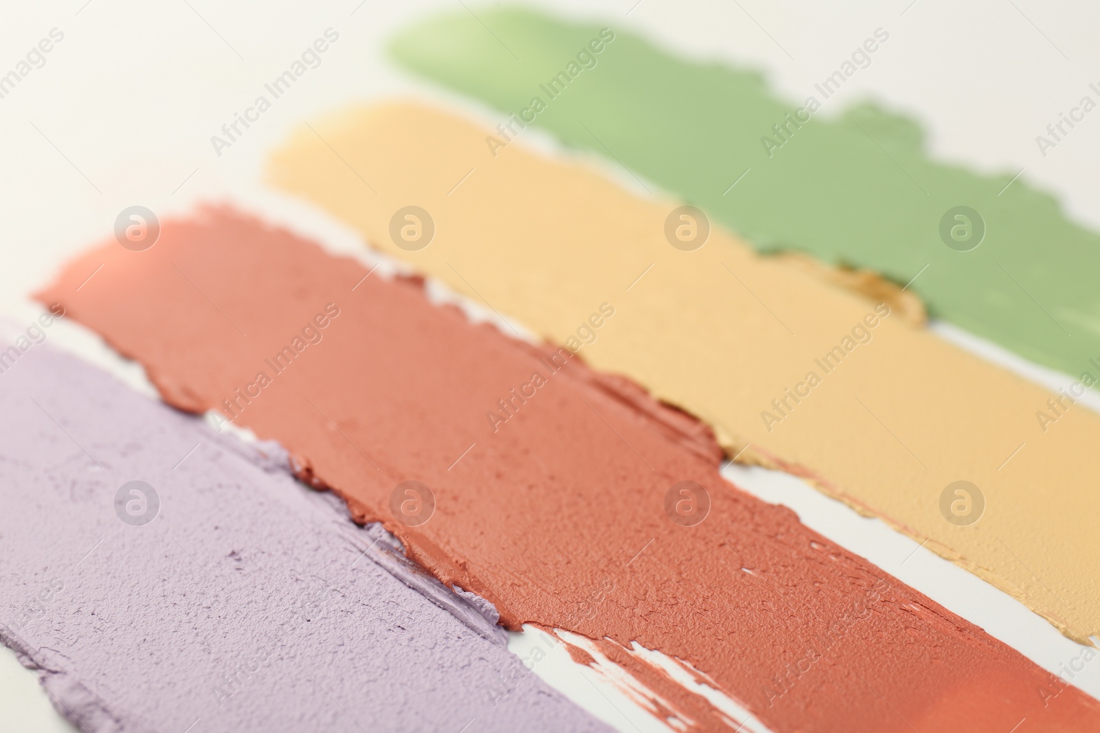 Photo of Samples of different color correcting concealers on white background, closeup