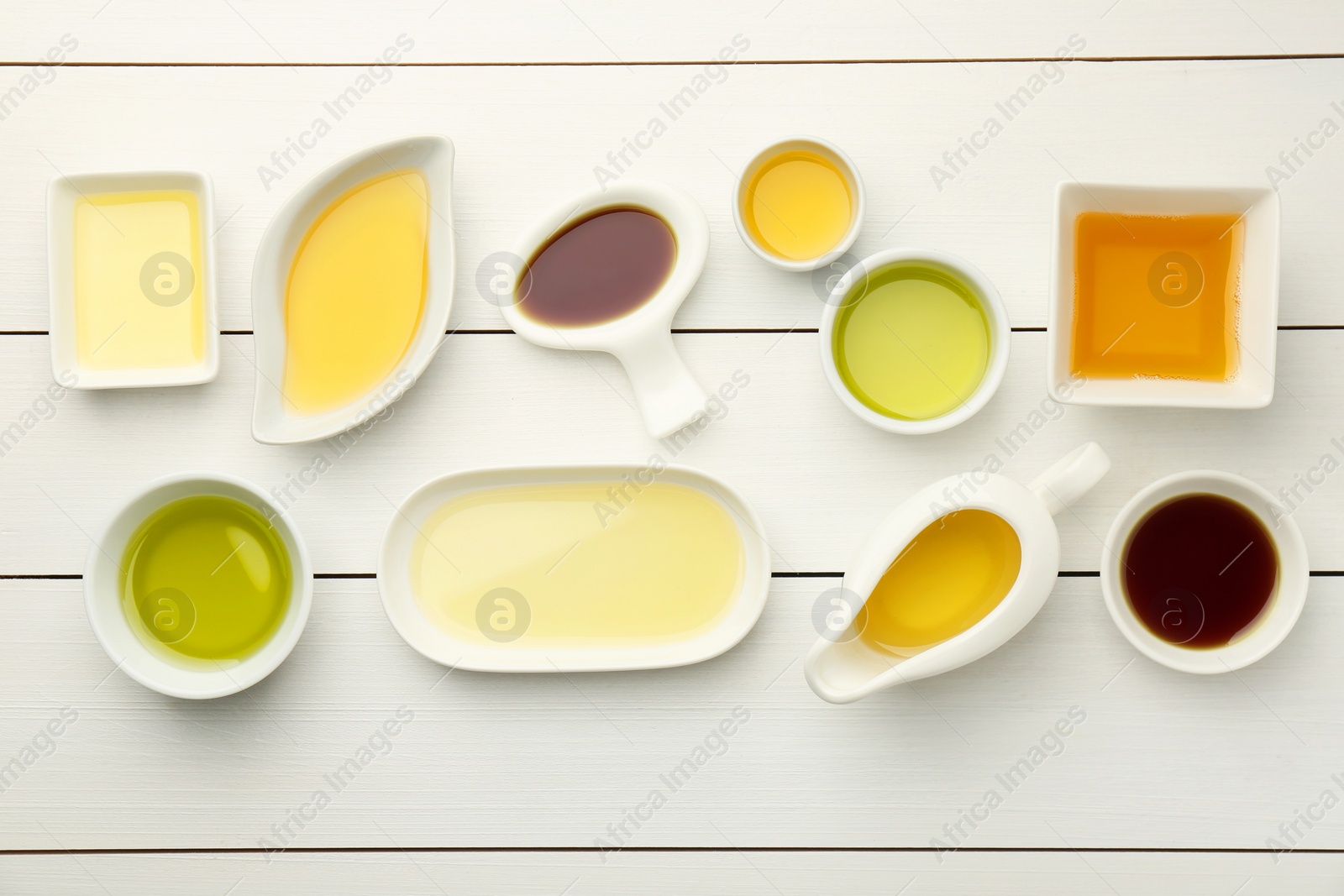 Photo of Vegetable fats. Different cooking oils on white wooden table, flat lay