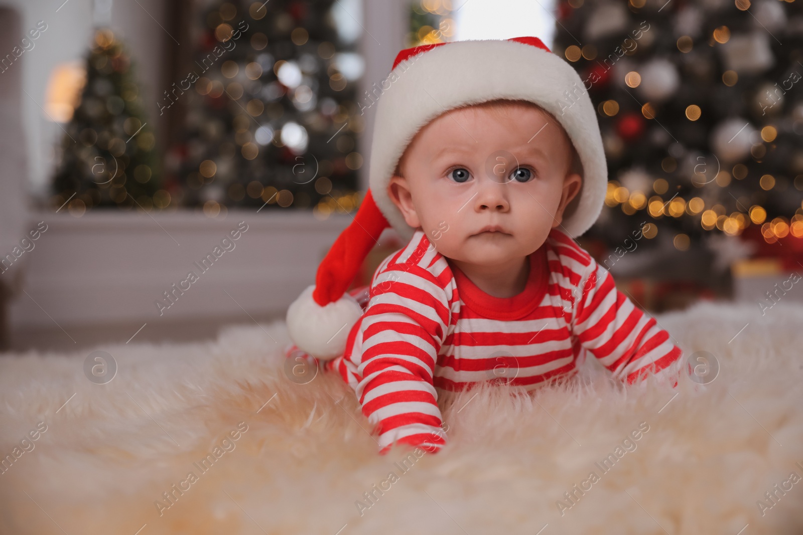 Photo of Cute little baby in bright pajamas and Santa hat on floor at home. Christmas suit