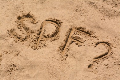 Abbreviation SPF and question mark written on sand at beach, above view
