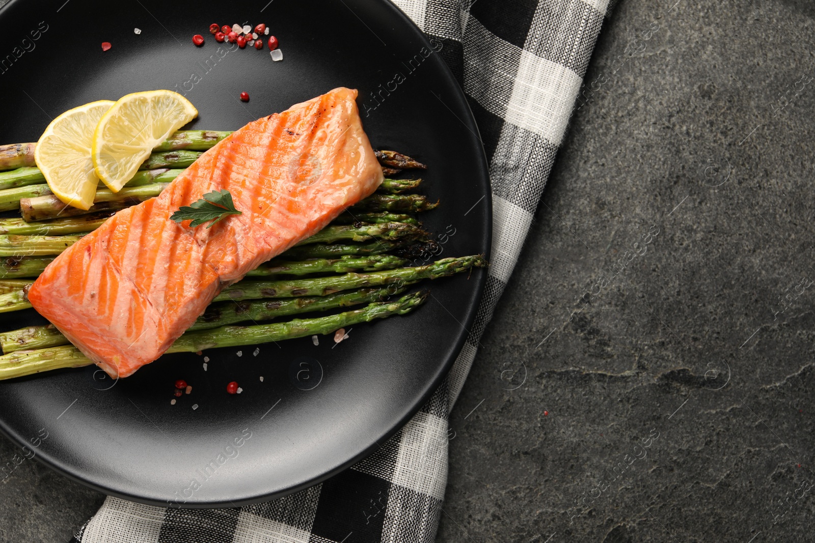 Photo of Tasty grilled salmon with asparagus, lemon and spices on gray table, top view. Space for text